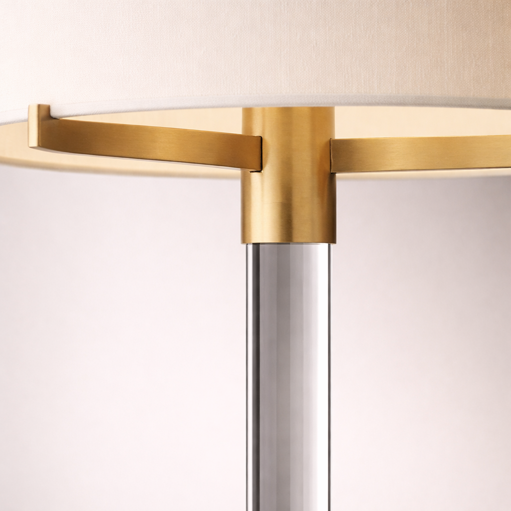 Close-up of the Clario aged brass crystal table lamp highlighting the white drum shade, aged brass hardware, and clear crystal stem
